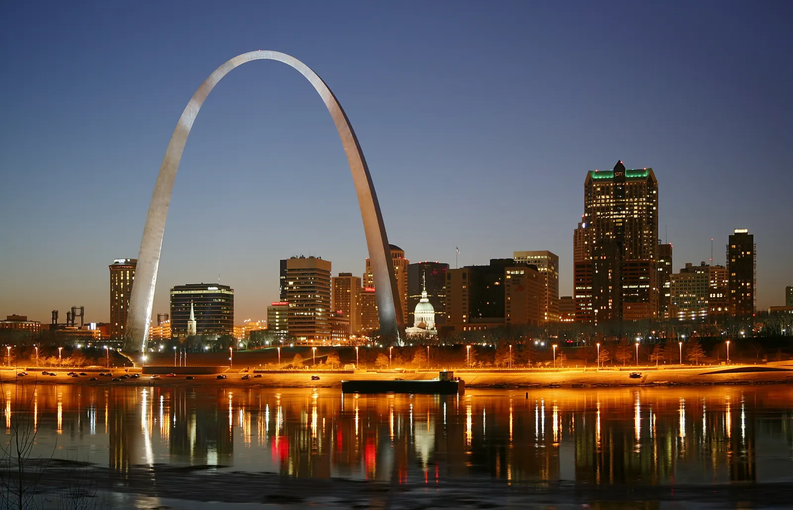 The Gateway Arch and downtown St. Louis lit up at dusk, reflected in the Mississippi River